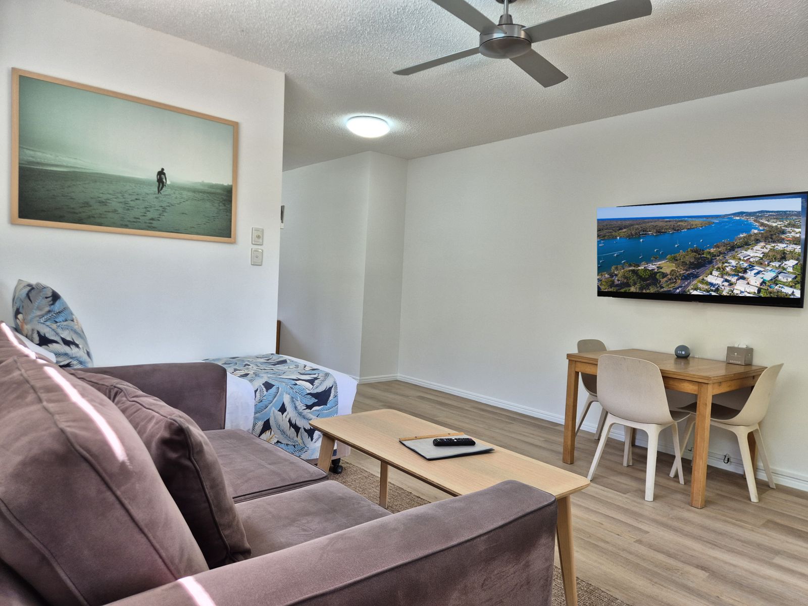 Living area with velvet lounge, single bed and dining table, with the Noosa River on the Smart TV