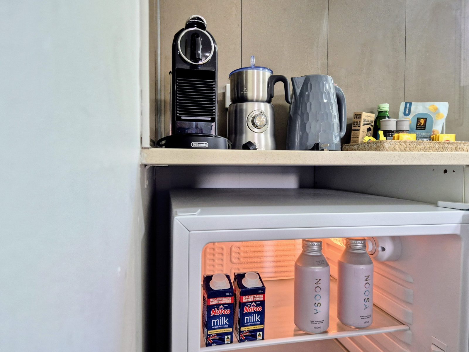 Coffee station with Nespresso machine, milk frother and kettle above a bar fridge stocked with Noosa spring water and milk