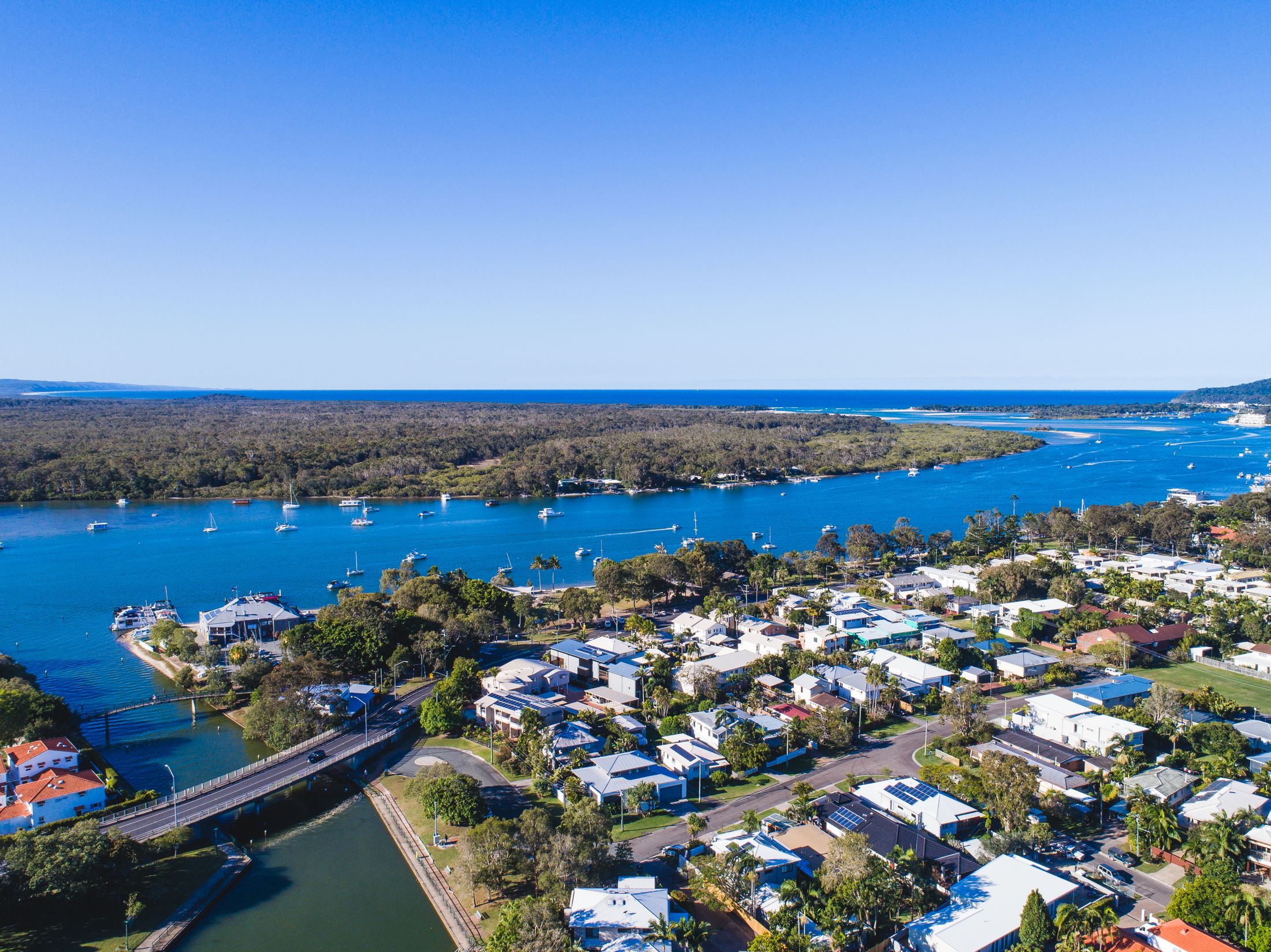 Aerial view of Noosaville and the Noosa River, with the canal and bridge in the foreground, boats on the river and the ocean beyond